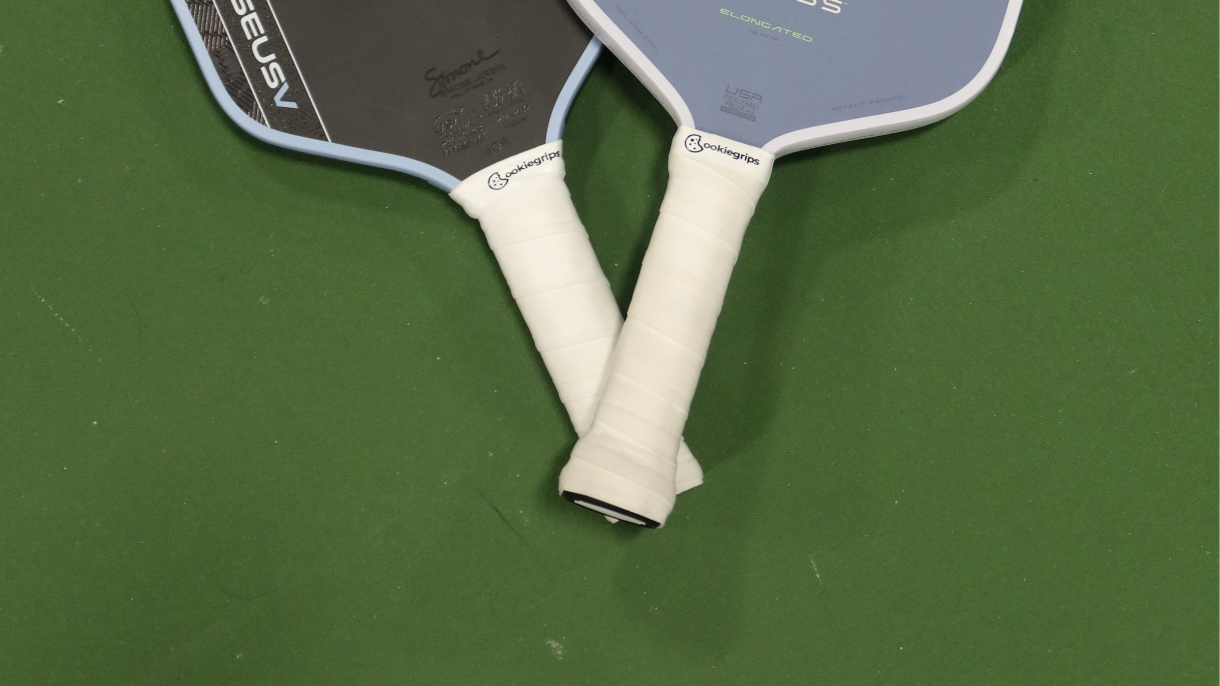 Two pickleball paddles with white handles wrapped with cookiegrips S'morey overgrip on a green surface