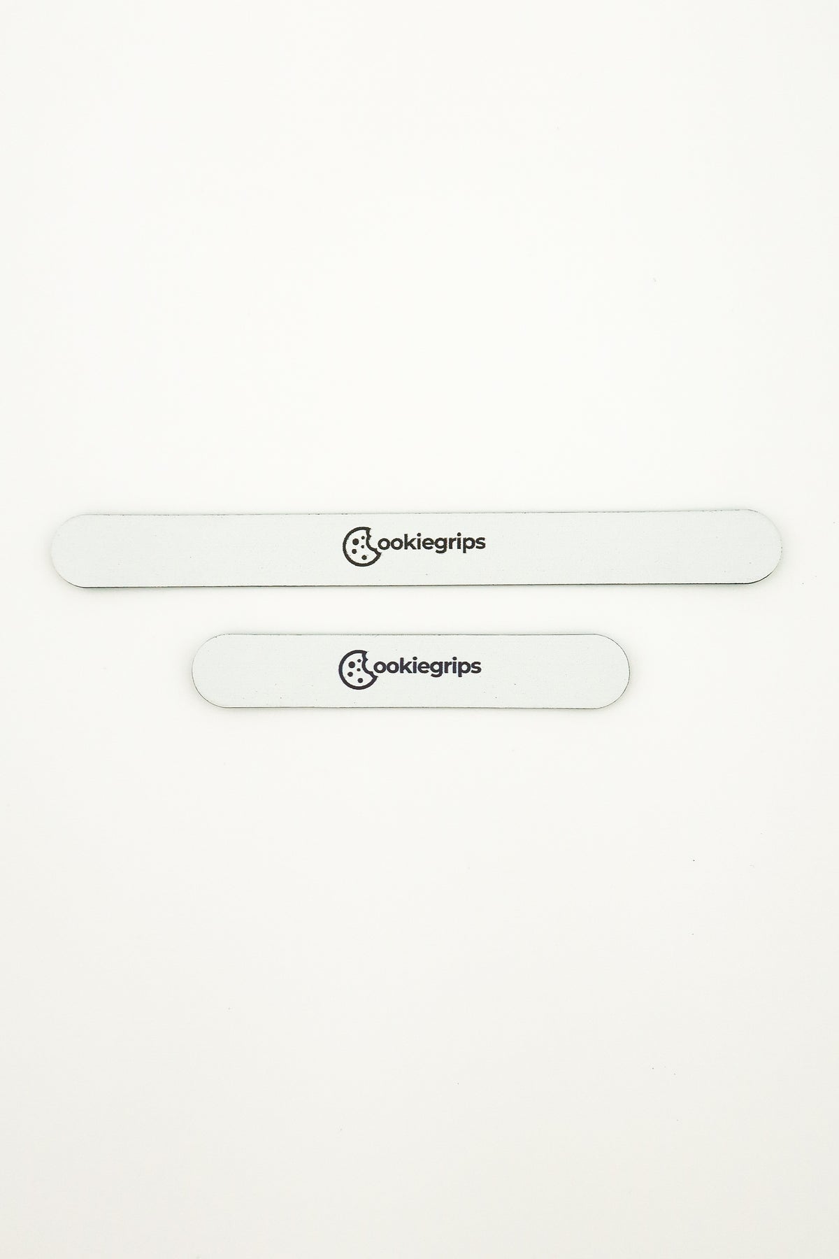 A long and a short Batter Bites pre-cut tuning strip, Sugar Glaze white with rounded ends and the black cookiegrips logo
