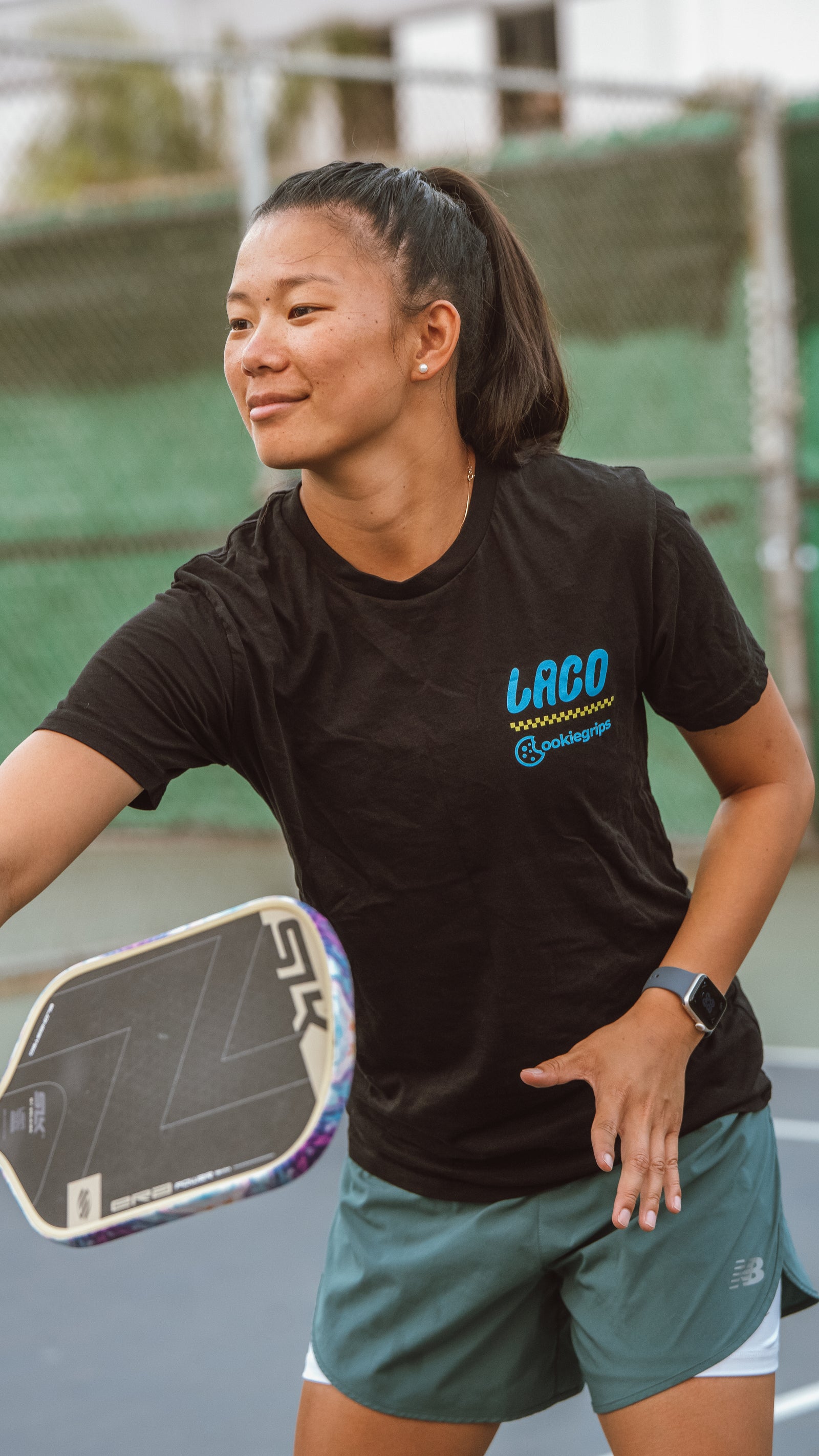 Woman holding a pickleball paddle in the black LACO x cookiegrips Now Serving T-shirt
