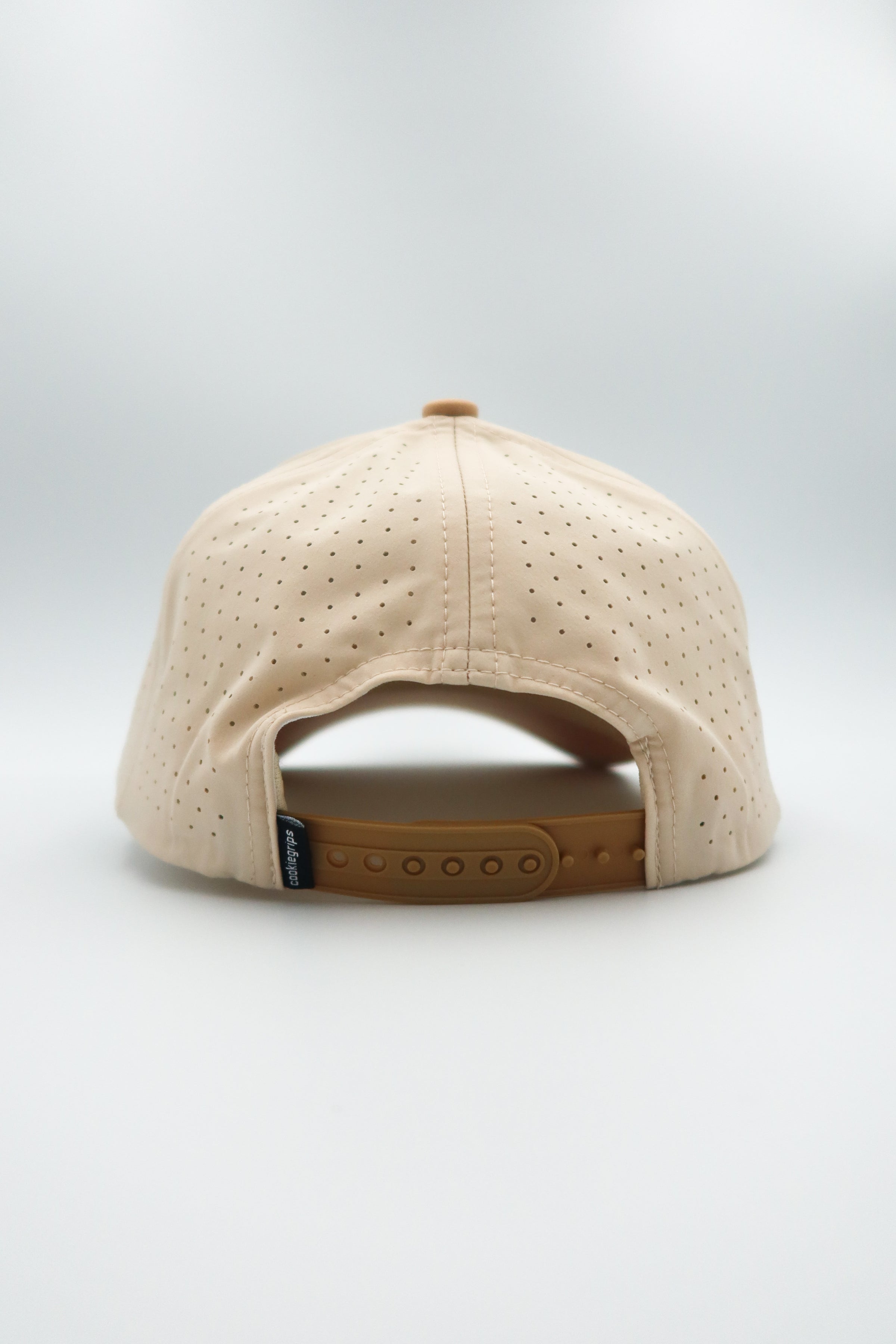 The back view of a beige baseball cap with perforated fabric panels and a tan adjustable strap, shown on a light gray background.