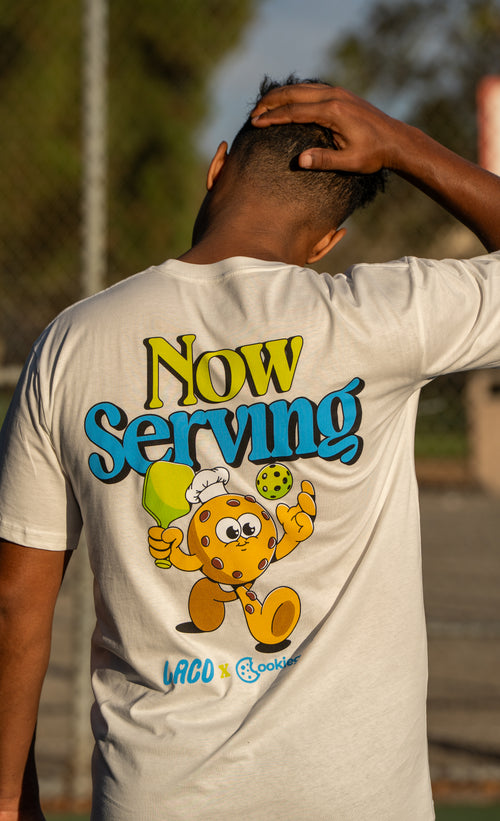 Back view of a man wearing the cream LACO x cookiegrips Now Serving pickleball T-shirt