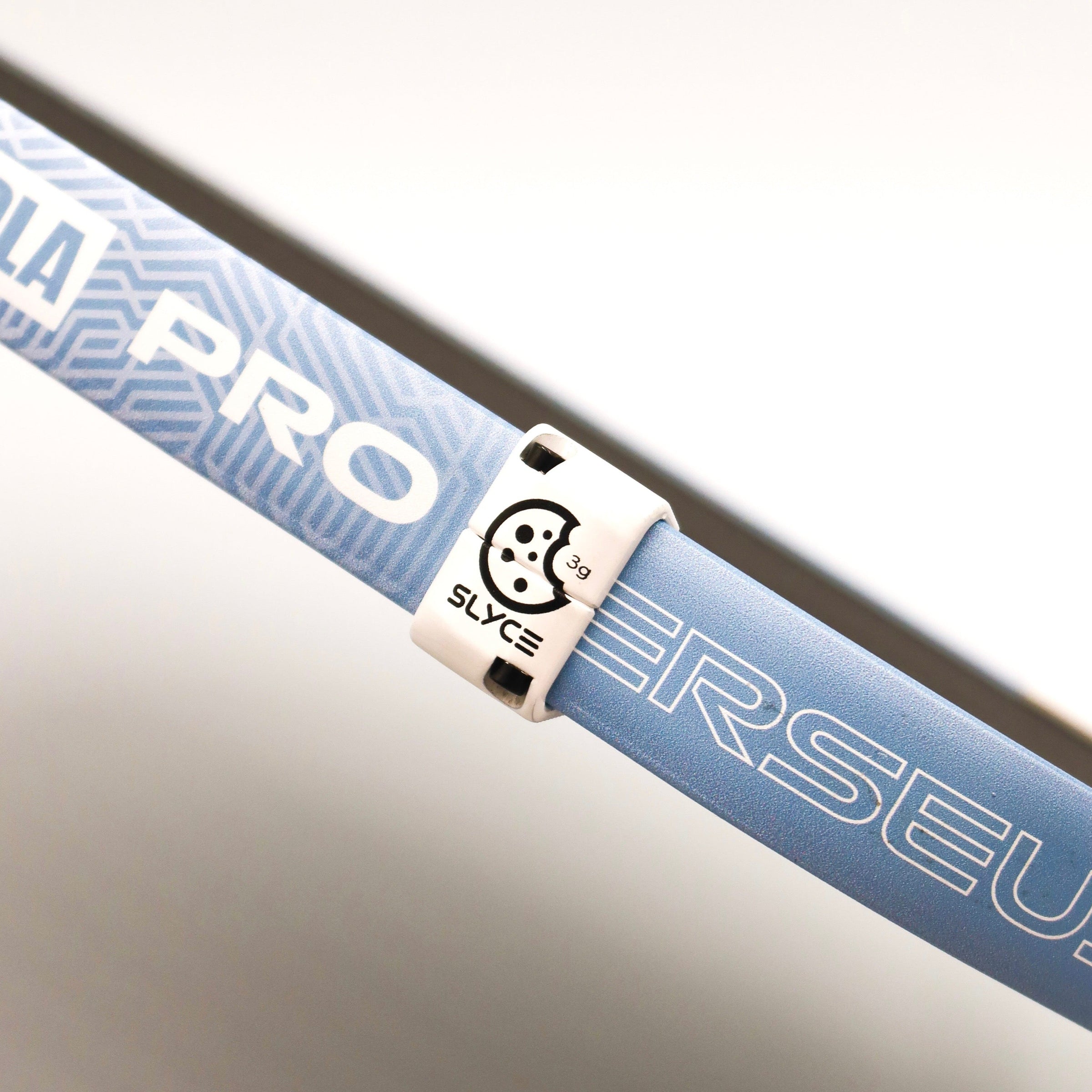 Close-up of a white cookiegrips x SLYCE SLYDR clamp weight on a blue and black pickleball paddle